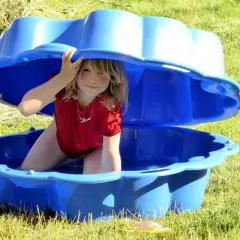 Niña sonríe bajo una tapa azul de arenero, disfrutando de actividades de verano. ¡Diversión acuática para niños de 2 años!