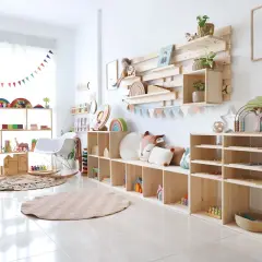 Acogedor rincón de juegos en el salón, con estanterías de madera llenas de juguetes educativos, cojines y una alfombra circular.