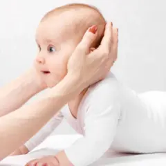 Manos sostienen la cabeza de un bebé que gatea. ¡Qué lindo mi bebe se pega en la cabeza!