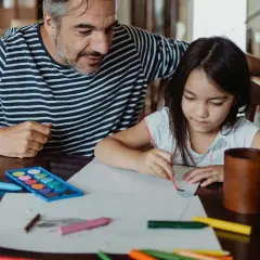 Padre e hija pintando con acuarelas y lápices de colores. Un momento de creatividad con materiales de escuela infantil.