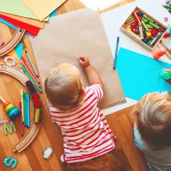 Dos niños pequeños disfrutan de actividades para niños de un año en guardería: pintan y juegan con un tren de madera.