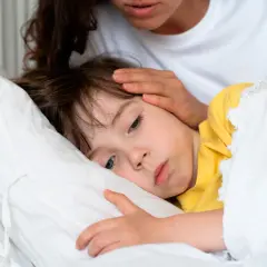 Madre reconforta a su hijo enfermo en la cama. Consejos sobre como calmar la tos en niños.