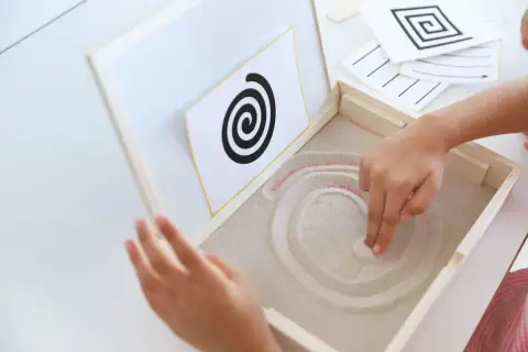 Niño practicando preescritura montessori, trazando espirales en arena.