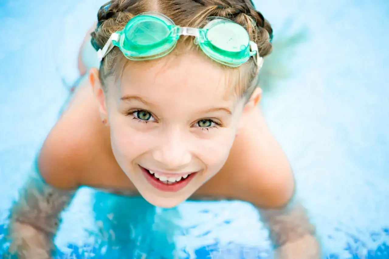 Ni&ntilde;a sonriente con gafas de nataci&oacute;n en la piscina, disfrutando de las actividades de verano.